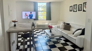 A living room with a checkered floor, a white sofa, a television, and a dining area with a table and chairs.
