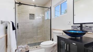 Une salle de bain moderne avec une douche à l’italienne en verre, des toilettes blanches et un lavabo noir avec un receveur bleu.