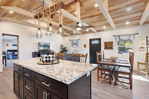A modern kitchen with a marble island, wooden ceiling beams, pendant lights, and a dining area with a wooden table and chairs. - Adorable 2-bedroom farmhouse in charming Placerville (Placerville)