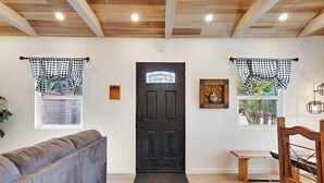 Um quarto com porta de madeira escura, cortinas xadrez, um sofá cinza, uma mesinha de madeira e uma cadeira de madeira.