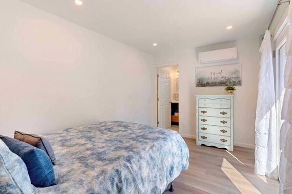 A bedroom with a bed, a dresser, and a door leading to another room.