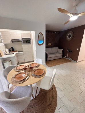 Une cuisine moderne avec des meubles blancs, une table à manger pour quatre personnes et un ventilateur de plafond.