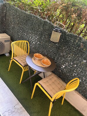 Eine Terrasse mit zwei gelben Stühlen, einem Tisch mit zwei Schalen und einer Hitachi-Klimaanlage.