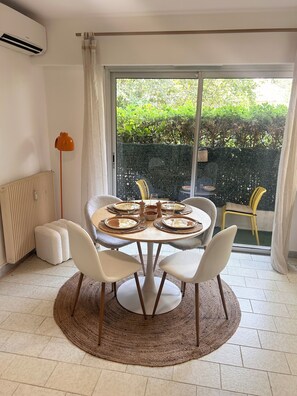 Ein Essbereich mit rundem Tisch, gedeckt für vier Personen, einem Heizkörper, einer Stehlampe und Blick auf einen grünen Garten durch ein großes Fenster.