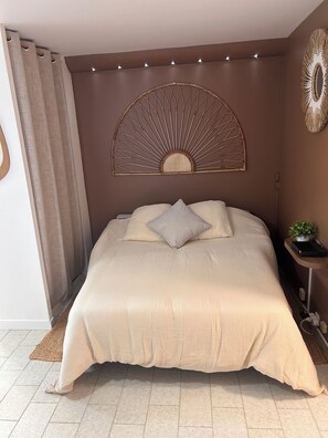 Ein ordentlich bezogenes Bett mit Kopfteil, ein Nachttisch mit Pflanze und ein an der Wand befestigtes dekoratives Element.