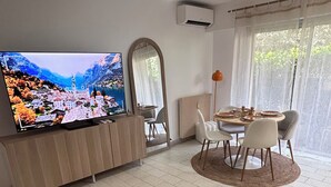 Una sala de estar con televisor, una mesa de comedor con sillas, un ventilador de techo y un espejo grande.