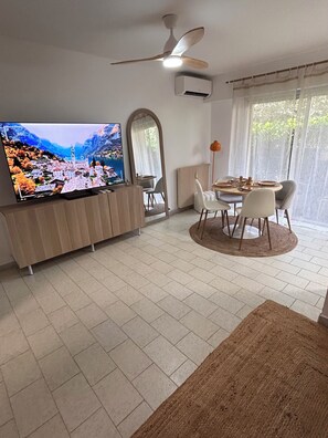 Ein Wohnzimmer mit Fernseher, einem Esstisch mit Stühlen, einem Deckenventilator und einem großen Spiegel.