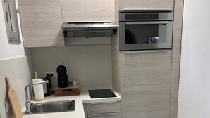 Una cocina compacta con horno integrado, cafetera y un cubo de basura.
