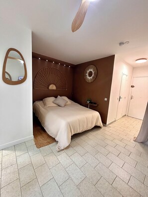 Ein Schlafzimmer mit einem Bett, einem Spiegel, einem Wandventilator und einer Tür.
