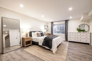 A modern bedroom with a large bed, bedside tables, a mirror, and a dresser. - Spacious 4BR Aurora Home with Sunroom and Fireplace (Aurora)