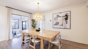 Een moderne eethoek met een houten tafel en stoelen, een hanglamp en een groot abstract schilderij aan de muur.