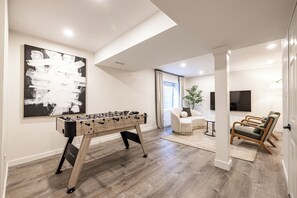 Ein modernes Wohnzimmer mit einem Kicker, einem großen abstrakten Gemälde und einer Sitzecke mit einer Couch und Sesseln.