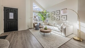 Een moderne woonkamer met een zwarte deur, een groot raam, een witte bank, een ronde salontafel en een vloerlamp.
