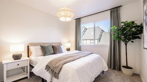 Een slaapkamer met een bed, nachtkastjes, een lamp, een potplant en een raam met gordijnen.