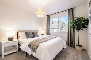 Ein Schlafzimmer mit Bett, Nachttischen, einer Lampe, einem Blumentopf und einem Fenster mit Vorhängen.