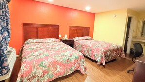 Habitación de hotel con dos camas, cabecera de madera, mesita de noche con lámpara y escritorio con silla.