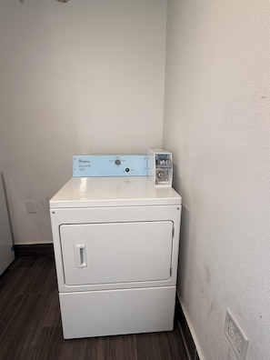 A front-loading white washer and dryer unit with a Whirlpool control panel, located in a corner of a room with a plain white wall and dark wooden flooring. - Budget Inn (Vidalia)