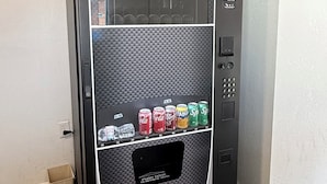 Máquina expendedora con aperitivos y bebidas, pantalla digital y puerta de acceso para retirar los productos.