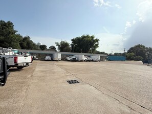 A parking lot with several trucks and trailers, a building with a blue roof, and trees in the background. - Budget Inn (Vidalia)