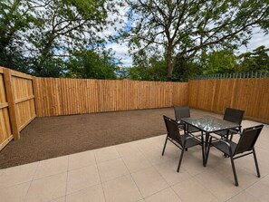 A patio with a wooden fence, a tiled floor, and a table with chairs. - The Riverside • 4 Bedroom 4 Bathroom • New Build House • Sleeps 7 • Driveway Parking • Yoko Property (Huntingdon)