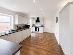 A modern kitchen with white cabinetry, a wooden floor, and a large window providing natural light. - The Riverside • 4 Bedroom 4 Bathroom • New Build House • Sleeps 7 • Driveway Parking • Yoko Property (Huntingdon)