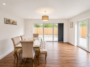 A dining area with a table and chairs, a pendant light, and a view through a glass door to an outdoor area. - The Riverside • 4 Bedroom 4 Bathroom • New Build House • Sleeps 7 • Driveway Parking • Yoko Property (Huntingdon)