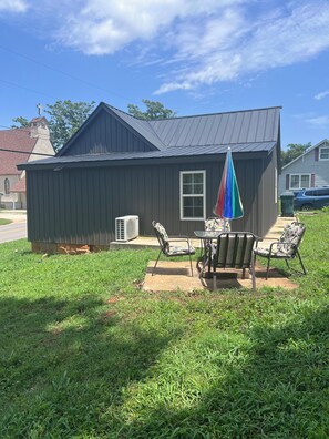 Une petite maison avec un toit en métal, une fenêtre et une terrasse avec deux chaises et une table.