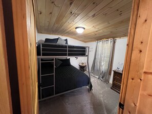 Een slaapkamer met stapelbed, een plafondlamp, een klein tafeltje met een kop en een bordje, en een gordijn.