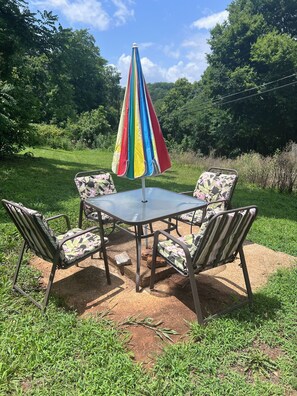 Een terras buiten met een tafel en stoelen, omringd door een gazon en bomen.