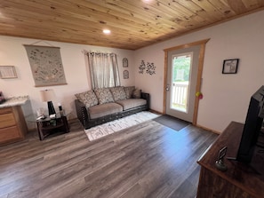 A furnished living room with a sofa, a coffee table, a television, and a door leading outside. - Cozy 2-bedroom house in Eminence with AC. Located in the heart of town!! (Eminence)