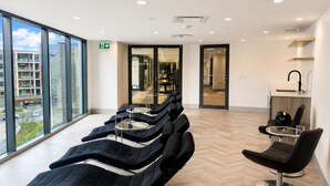 Un área de espera moderna con sillones de masaje, una recepción y grandes ventanales con vistas a la ciudad.