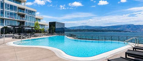 Zwembad met uitzicht op bergen en een waterpartij, omringd door ligbedden en een modern gebouw.