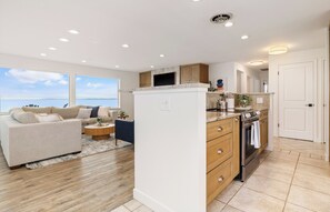 A modern kitchen with a built-in oven and microwave, wooden cabinets, and a view of the sea through large windows. - Whidbey Island Updated Beachfront Getaway - A View From Every Room! (Oak Harbor)