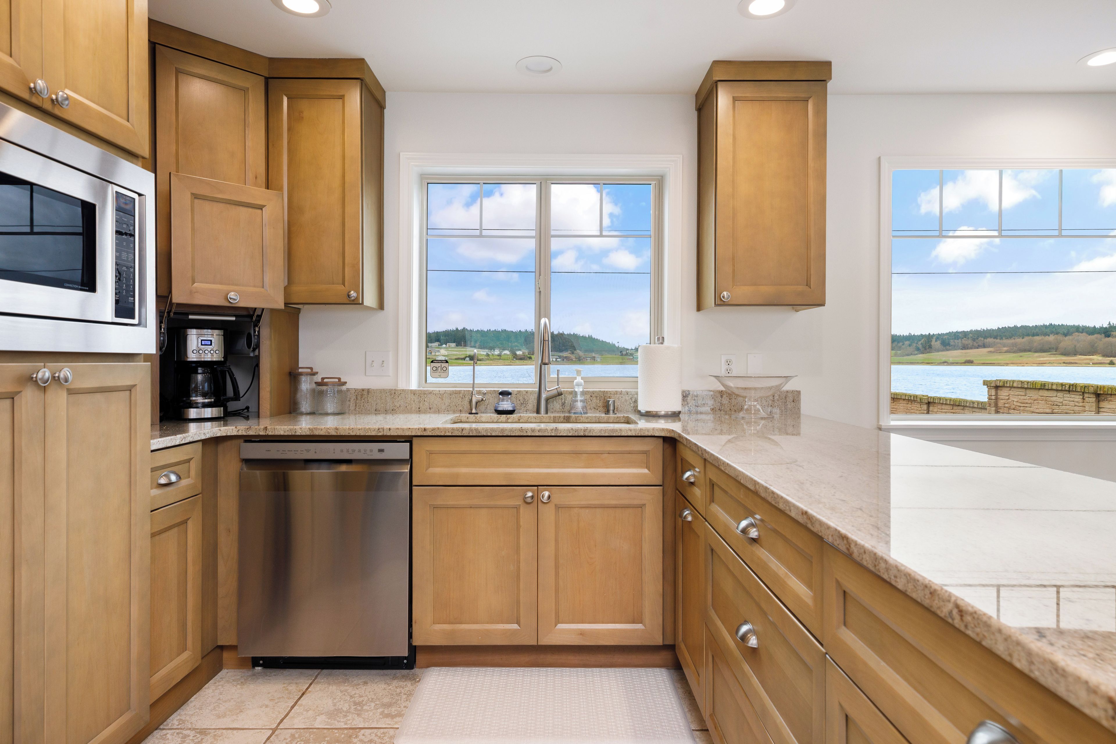 A kitchen with wooden cabinets, stainless steel appliances, a dishwasher, and a window with a view of a lake.