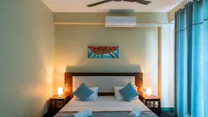 A hotel room with a bed, two bedside tables, a ceiling fan, an air conditioning unit, and a window with curtains. - Hotel Velmont Kandy (Kandy)
