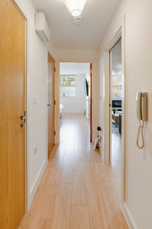 A hallway with wooden flooring, white walls, and a ceiling light. - Modern 1BR | Sleeps 6 | Free Parking (London)