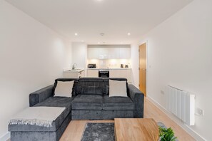 Ein modernes Wohnzimmer mit einem grauen Ecksofa, einem Holztisch und einem grauen Teppich.
