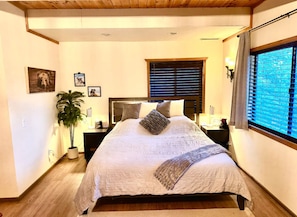 A bedroom with a large bed, a window with blinds, a potted plant, and wall-mounted artwork. - Cozy place close to ski resorts, lake, town & golf (Big Bear)