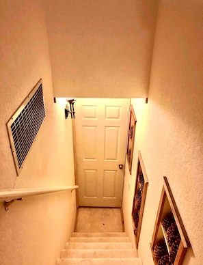 Uma escadaria que leva a uma porta, com um respiradouro na parede e quadros nas laterais.