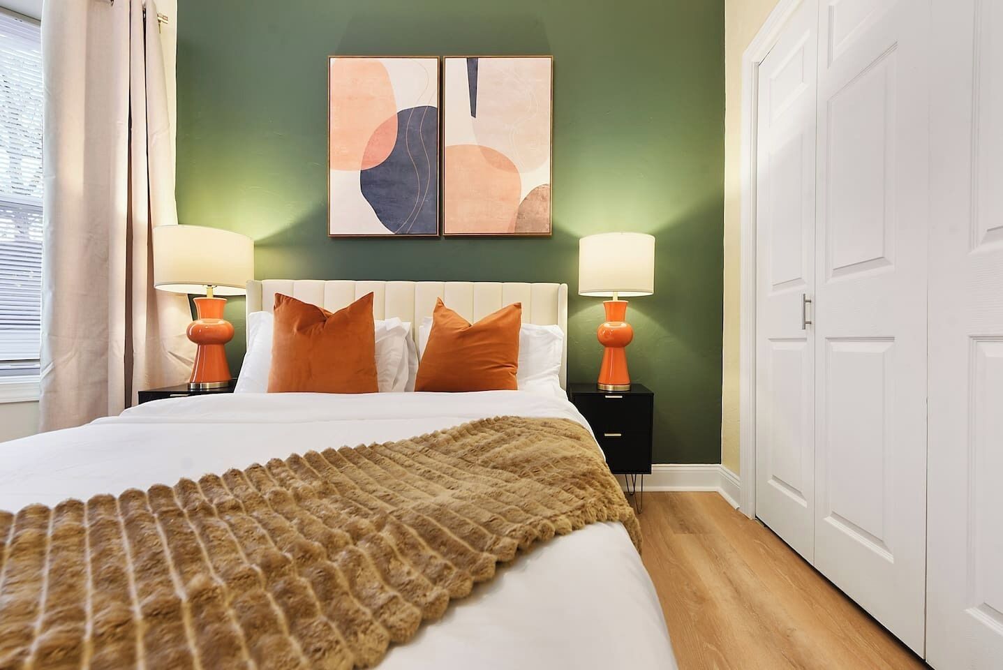 Modern bedroom with orange accents, white headboard, and bold artwork.