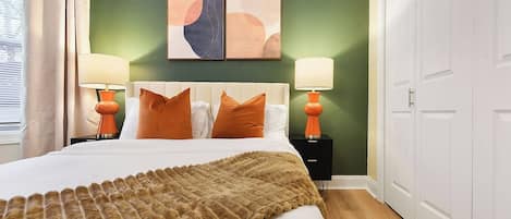 Modern bedroom with orange accents, white headboard, and bold artwork.