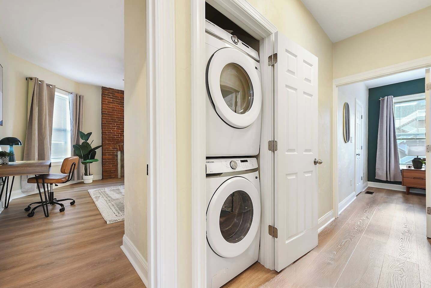 Une buanderie équipée de deux machines à laver et deux sèche-linge à chargement frontal superposés, avec un plancher en bois et un mur en briques.