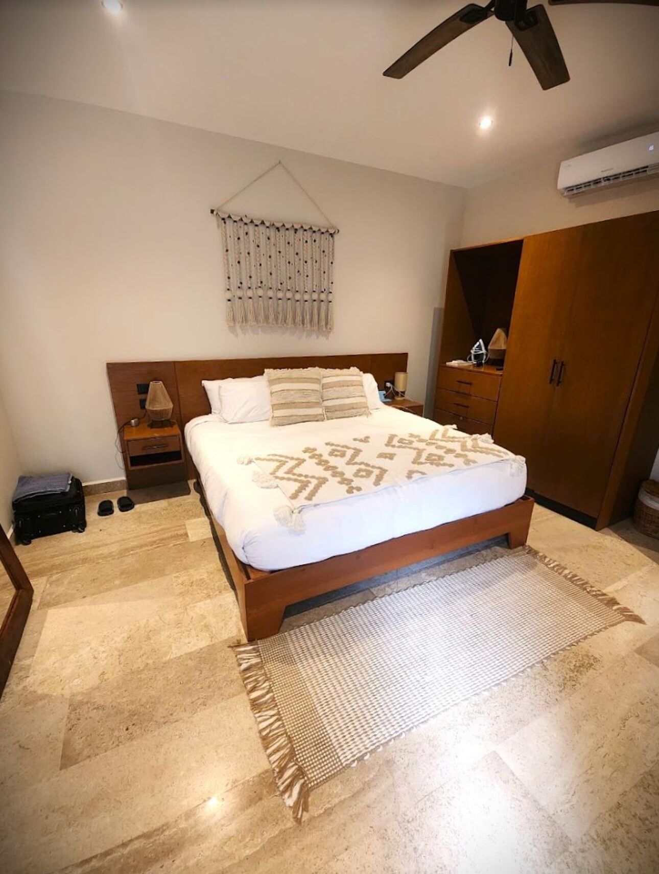 A bedroom with a bed, bedside tables, a hanging decor, a wardrobe, and a ceiling fan.