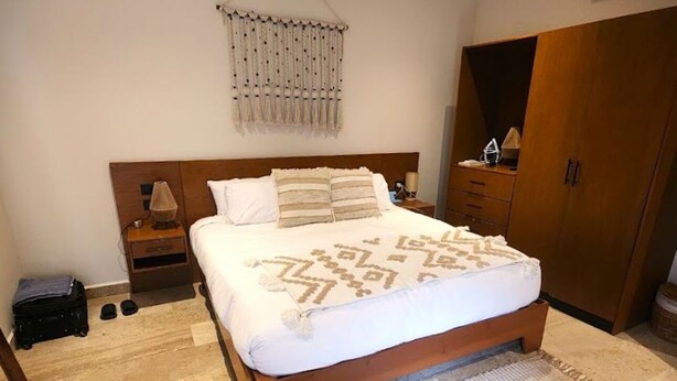 Une chambre à coucher comprenant un lit, des tables de chevet, un élément de décoration suspendu, une armoire et un ventilateur de plafond.