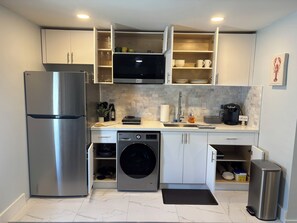 Cocina compacta con refrigerador de acero inoxidable, microondas integrado y lavadora.