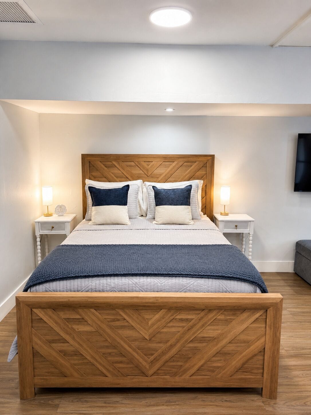 A neatly arranged bedroom with a wooden bed frame, a headboard, two bedside tables with lamps, and a wall-mounted TV.