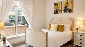 A bedroom with a white bed, a bedside table with a lamp, and two paintings on the wall. -     Luxury River Walk Retreat 2BR Downtown (San Antonio)