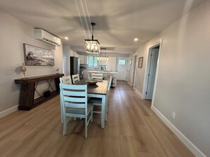 A spacious kitchen with modern appliances, a dining area with white chairs, and a hallway leading to bedrooms.