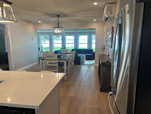A modern kitchen with a central island, dining area with chairs and a table, and a living room with a sofa and a coffee table.