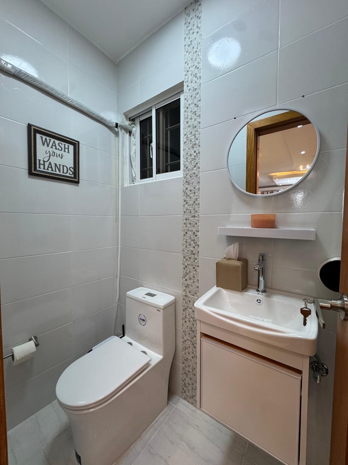 Une salle de bain avec des toilettes, un lavabo et un panneau indiquant : « Lavez-vous les mains ».
